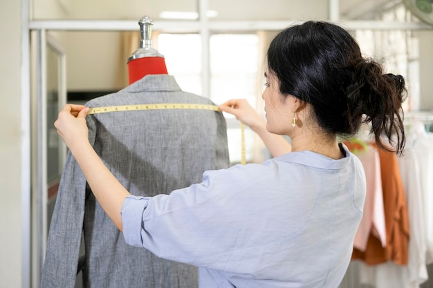 Closeup young woman tailor taking measurements of jacket on mannequin.