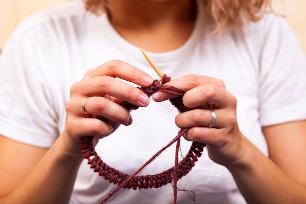 Closeup of an young woman in white tshirt and jeans knits a natural wool brown hat with knitting needles