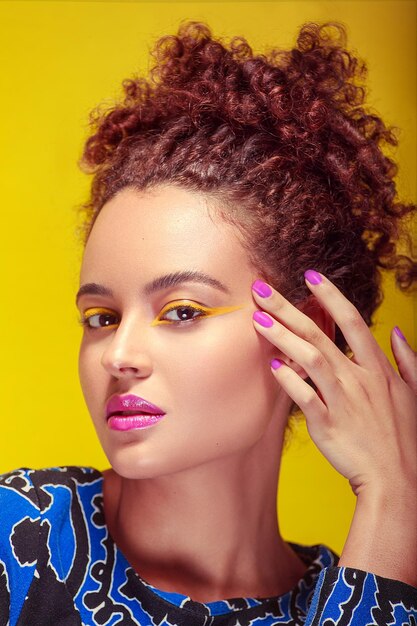 Closeup of a young womans face with tightly curled hair yellow makeup and a blue