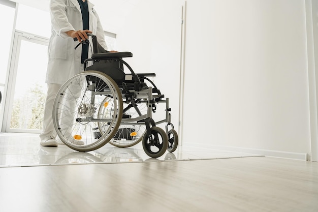 Closup of professional male doctor holding wheelchair in hospital clinic hall