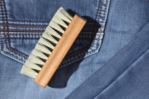 A clothes brush lies on folded jeans.