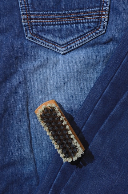 A clothes brush lies on folded jeans.