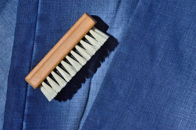 A clothes brush lies on folded jeans.