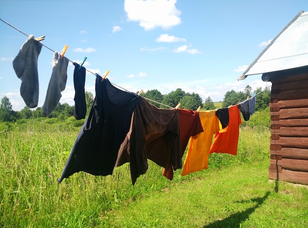 Photo clothes hanging on washing line against a blue sky and green field. washing line with drying clothes in courtyard.