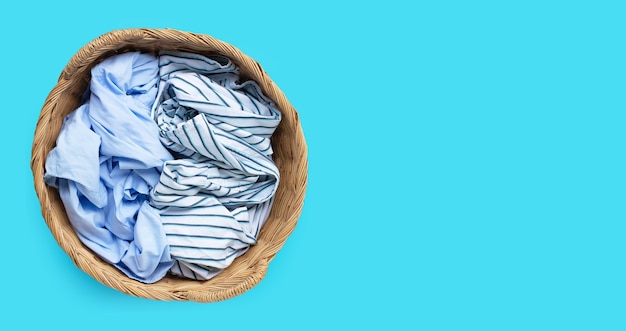 Clothes in laundry basket on blue background. Copy space