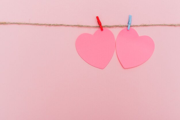 Clothes pegs and red paper hearts on rope isolated on pink background