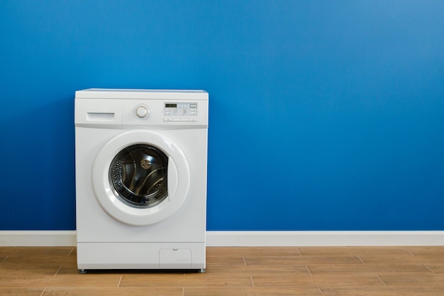Clothes washing machine in laundry room interior on blue wall, copy space