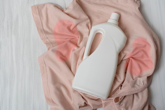 Clothes with stains and a bottle of detergent. Top view