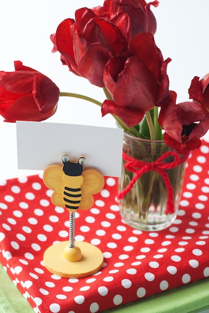 A clothespin for notes in the form of a bee stands next to a bouquet of red tulips