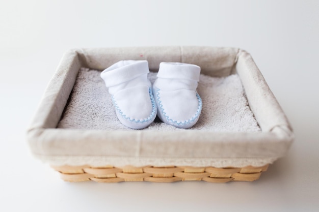 clothing, babyhood, motherhood and object concept - close up of white baby bootees for newborn boy on towel in basket