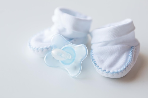 clothing, babyhood, motherhood and object concept - close up of white baby bootees and soother for newborn boy