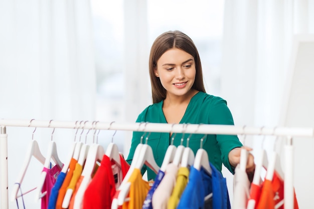 clothing, fashion, style and people concept - happy woman choosing clothes at home wardrobe