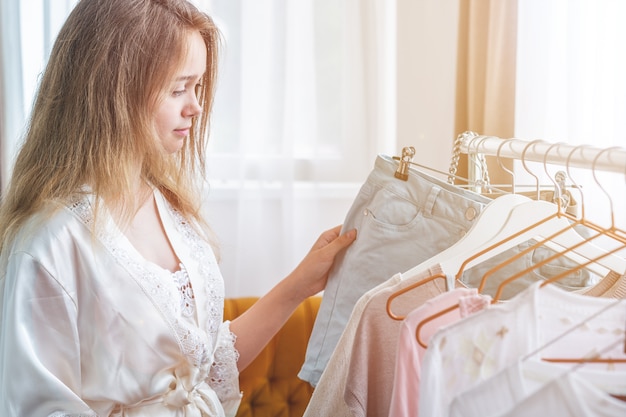 Concetto dell'abbigliamento, di modo, di stile e della gente - donna che sceglie il guardaroba dei vestiti a casa