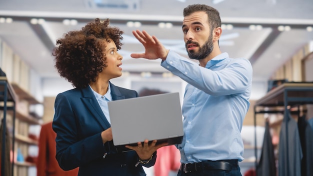 Foto una donna d'affari di un negozio di abbigliamento usa un computer portatile parla con uno specialista di merchandising visivo collabora per creare una collezione elegante piccola impresa direttore delle vendite di una boutique di moda parla con un designer