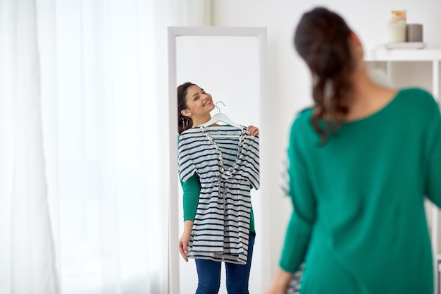 clothing, wardrobe, fashion, style and people concept - happy woman with shirt looking to mirror at home