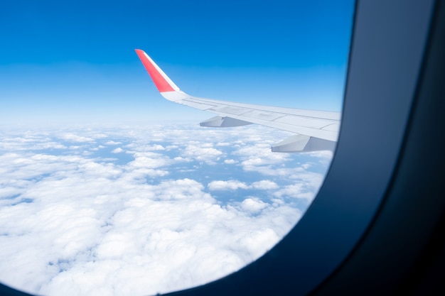 航空機の窓から雲、青空、飛行機の翼が見えてきました。