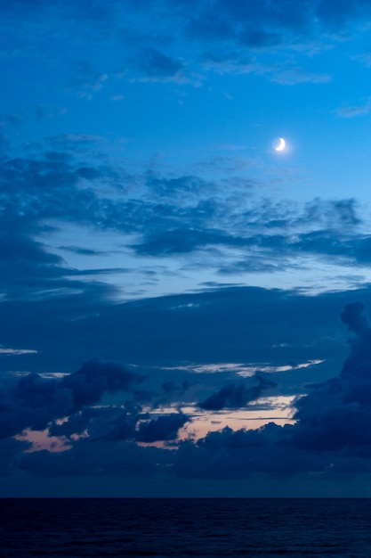 Cielo blu navy di sera della nuvola con una luna crescente sopra la superficie del mare.