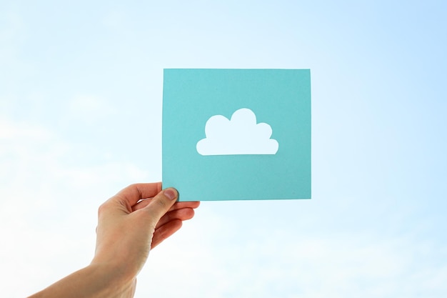 A cloud is cut out of paper in a hand against the background of the sky