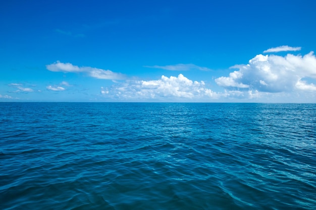 Photo clouds on blue sky over calm sea with sunlight reflection