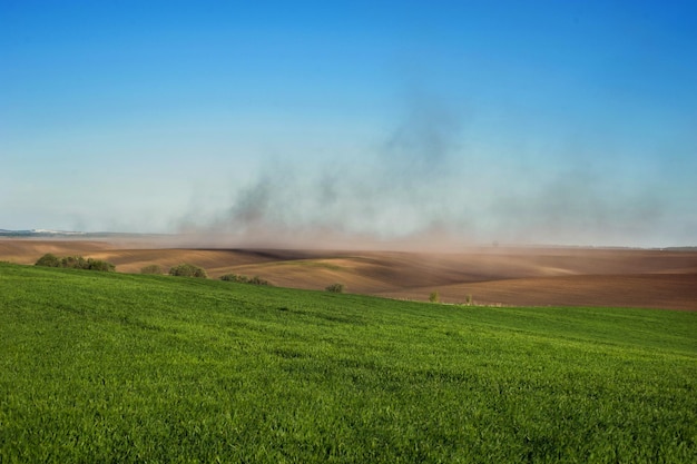 Clouds of dust on the hills of plowed lands, green fields winter wheat and problem of soil erosion from the wind