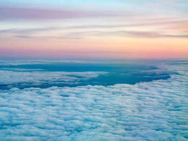 自然な夕暮れの光の下で航空機の窓からの雲の上