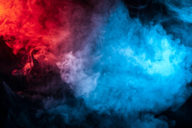 Photo clouds of isolated colored smoke blue red orange pink scrolling on a black background in the dark close up