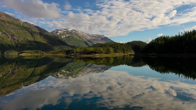 Облака горы и лес отражаются в озере как в зеркале.