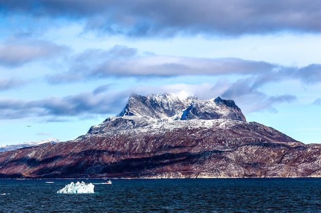 グリーンランドのヌーク市近くの前景に青い海と雪に覆われた Sermitsiaq 山の頂上の雲