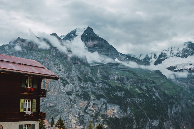 Clouds snow peaks and traditional house chalet in Jungfrau mountains Swiss Alps