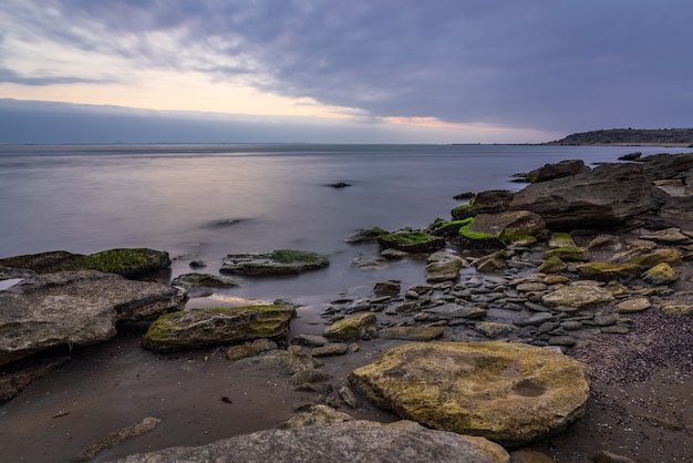 Cloudy sunrise on rocky sea coast, long exposure