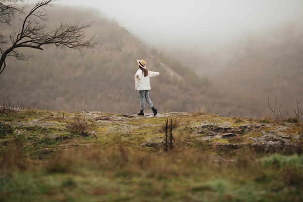 Cloudy weather, calm atmosphere. The happy girl with hands up travels through the mountains.