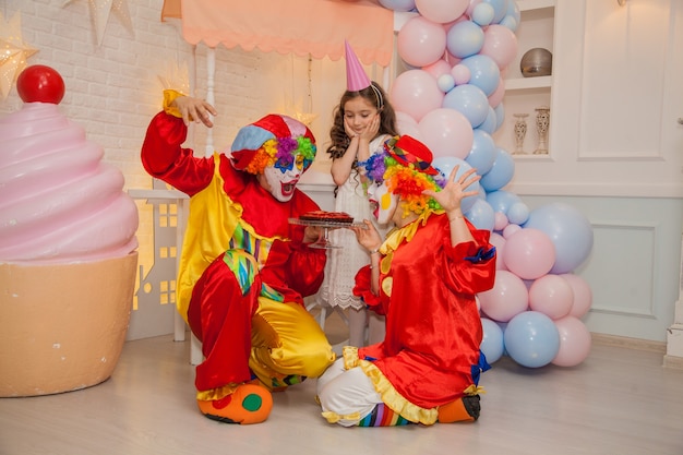 Clown boy and clown girl at girls birthday party blowing cake