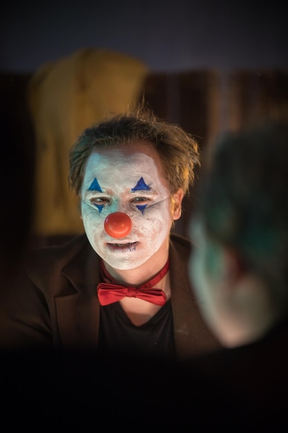 Clown concept a man with cracked painted face looking in the mirror