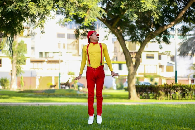 Clown trying to jump in a park red pants yellow shirt