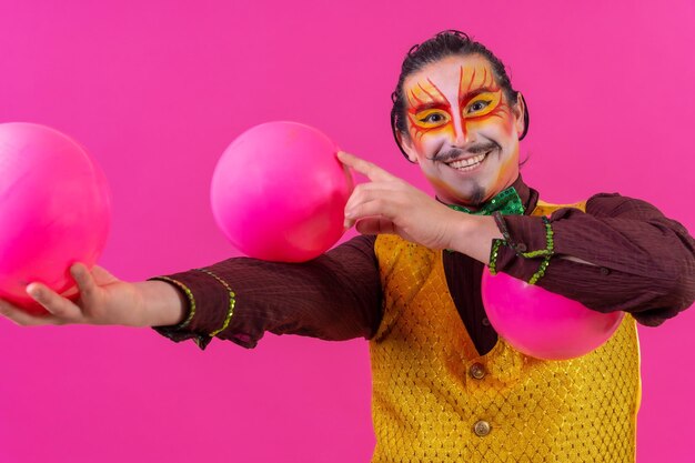 Clown with white facial makeup on a pink background juggling balls