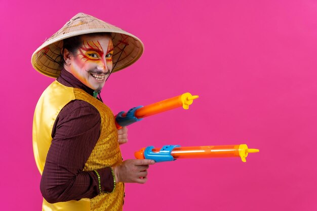 Clown with white facial makeup on a pink background with toy guns