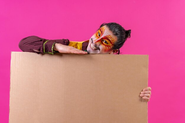 Clown with white facial makeup showing a sign on a pink background announcing something