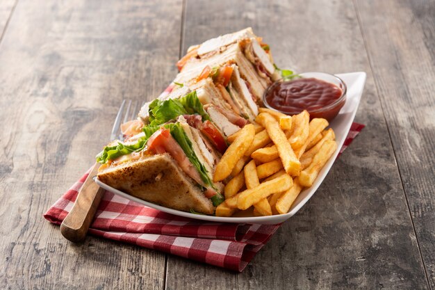 Club sandwich and French fries with ketchup sauce on wooden table