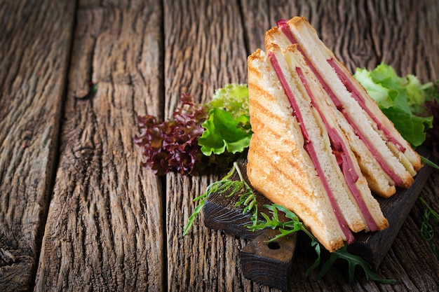 Club sandwich - panini with ham and cheese on wooden background. Picnic food.