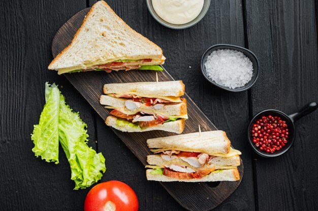 Panini sandwich club con prosciutto, pomodoro fresco, formaggio, sulla tavola di legno nera, vista dall'alto