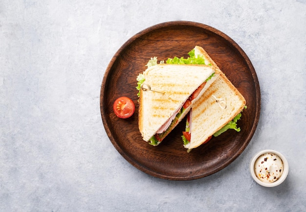 Club sandwich on a wooden plate of ham cheese cucumber tomato and lettuce leaves on a blue background with mayonnaise Top view and copy space