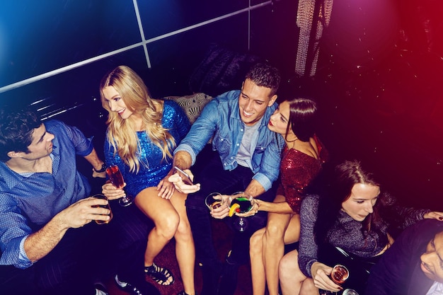 Фото Клубный диван, алкогольный коктейль и друзья празднуют новый год со счастливым часом, пьют энергию или музыку для вечеринок. общение в ночном клубе, разговоры и вид сверху.