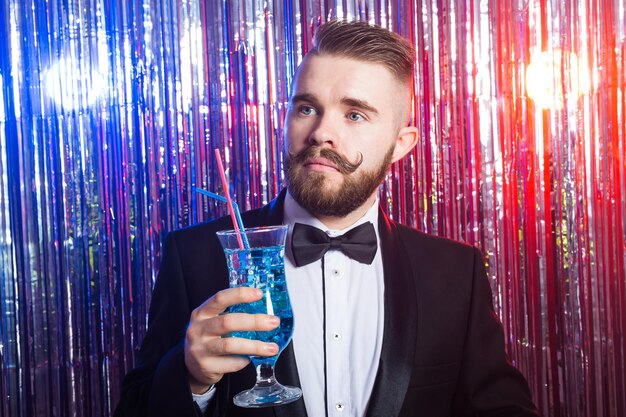 Clubfeest en vakantie concept - portret van elegante knappe man in een duur pak houdt blauwe cocktail vast op glanzende achtergrond.