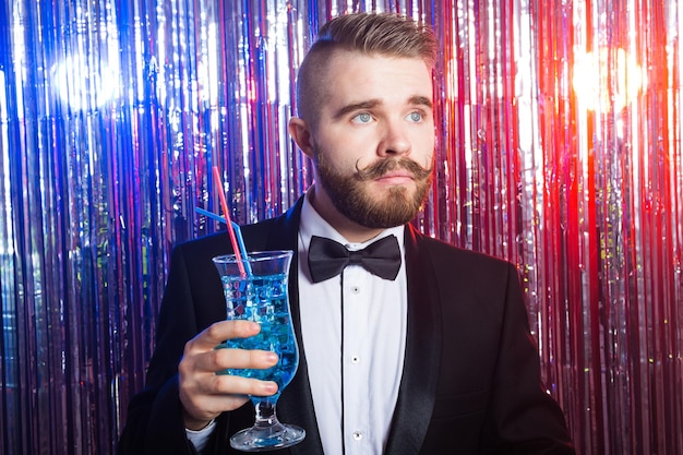 Clubfeest en vakantie concept - portret van elegante knappe man in een duur pak houdt blauwe cocktail vast op glanzende achtergrond.