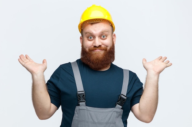 흰색 배경에 고립 된 빈 손을 보여주는 카메라를보고 안전 헬멧과 유니폼을 입고 단서가없는 젊은 남성 건설 노동자