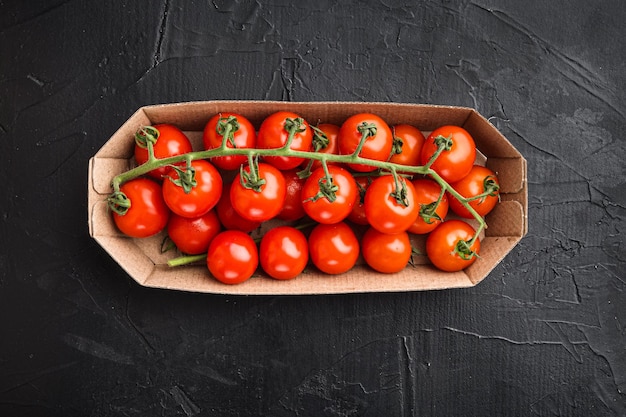 Cluster of fresh red cherry tomatoes in container on black stone background top view flat lay