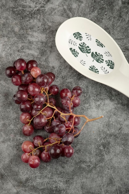 Cluster of red grapes and empty white plate on marble surface. 