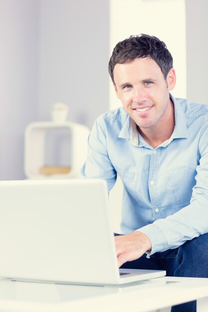 Cmiling casual man looking at camera using laptop