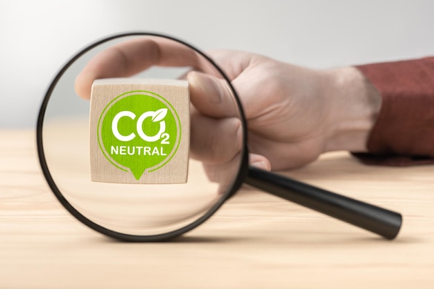 Co2 neutral sign through magnifying glass on table co2 neutral\
written on wooden blocks reduce global warming concept reduce\
carbon dioxide emissions and limit global warming and climate\
change