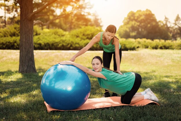 Тренер помогает женщине в зеленой футболке выполнять упражнения йоги.
